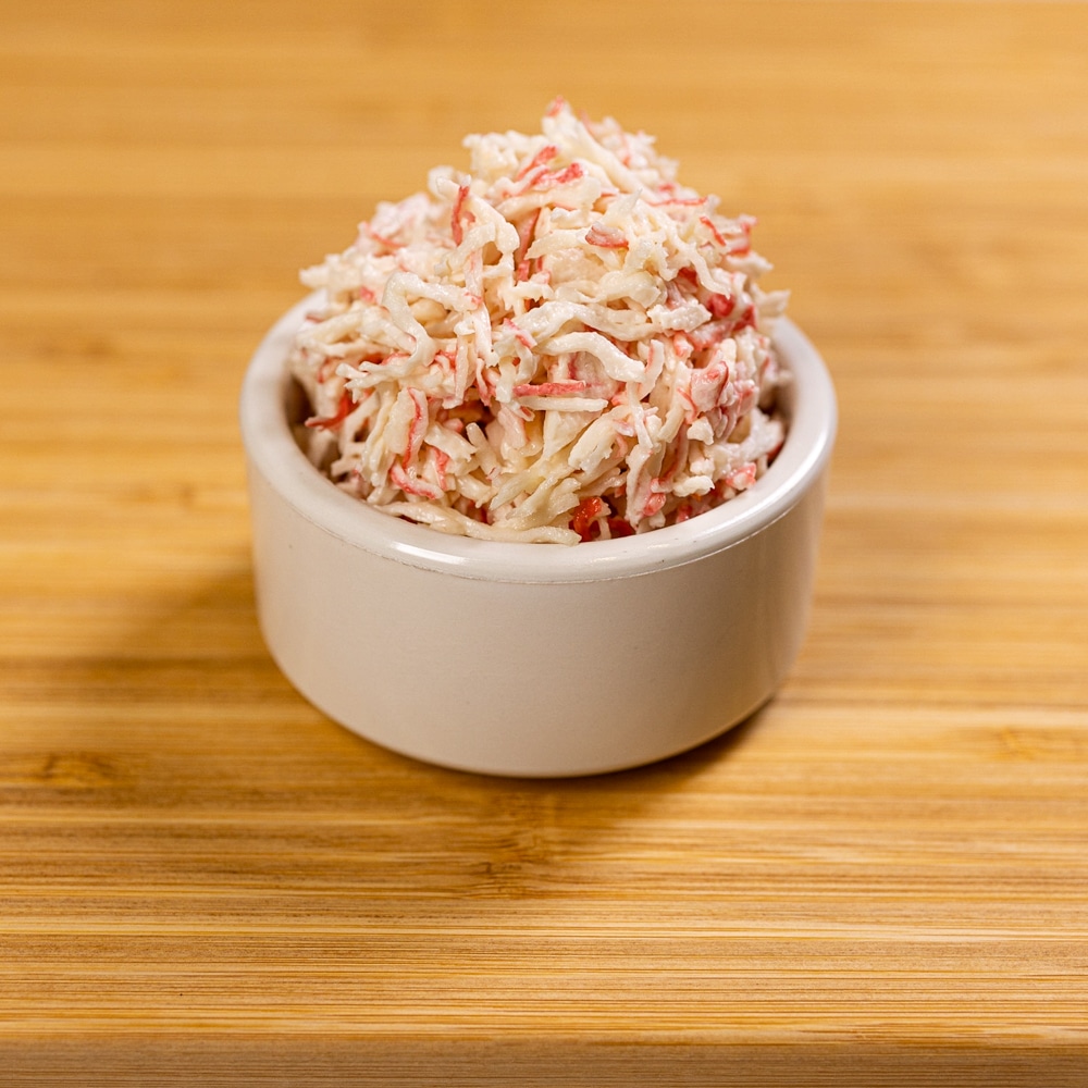 A bowl of shredded carrots on top of a wooden table.