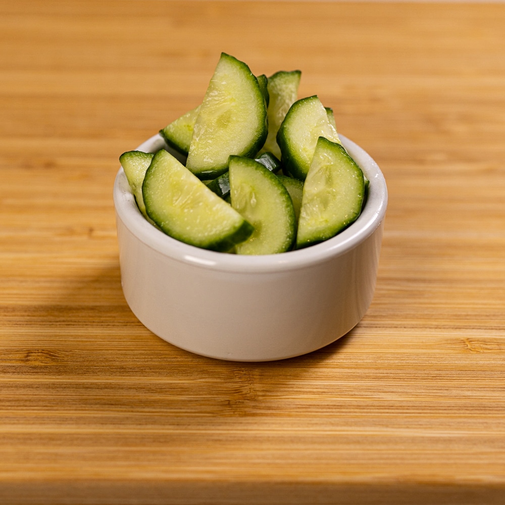 A bowl of cucumbers on a wooden table.