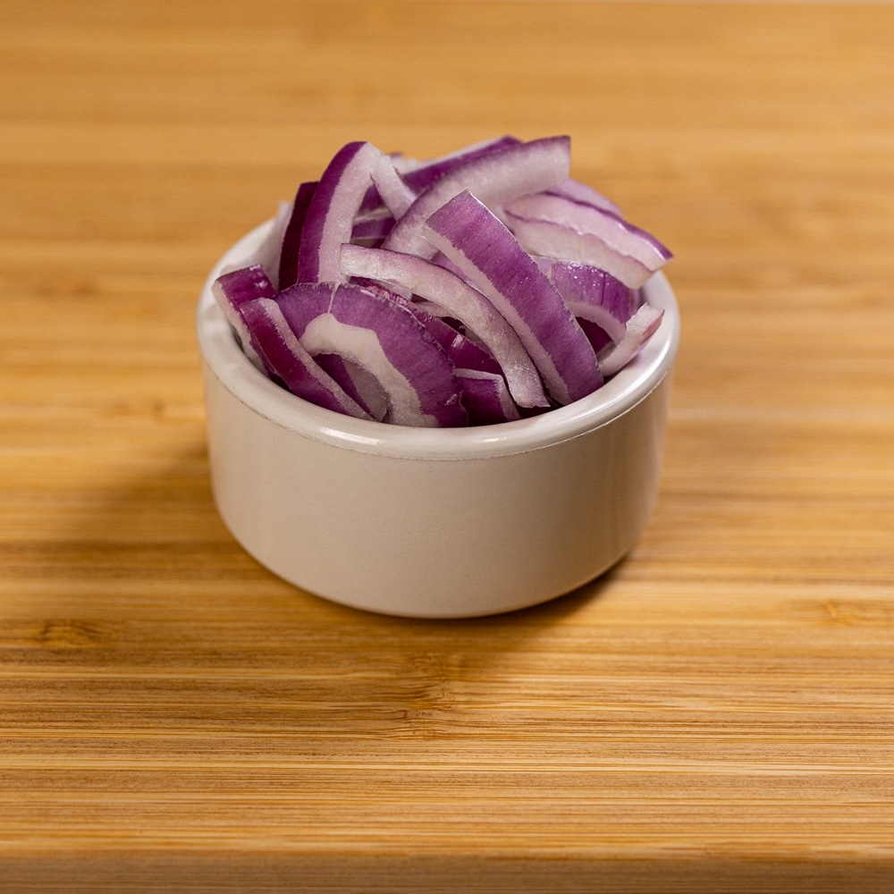 Sliced red onions in a white bowl on a wooden table.