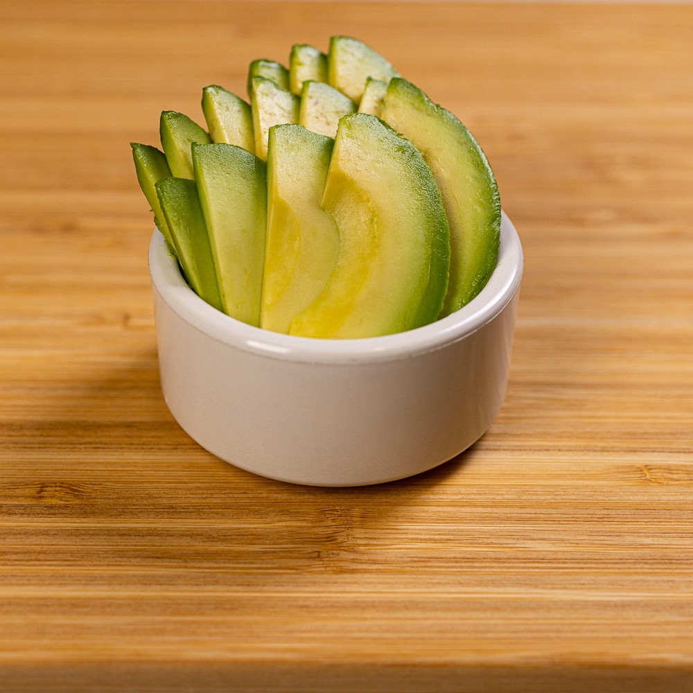 Sliced avocado in a bowl on a wooden table.