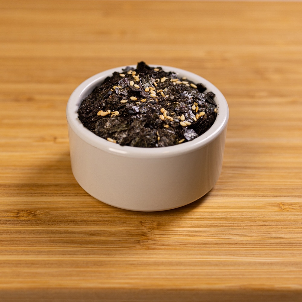 A bowl of black sesame seeds on top of a wooden table.