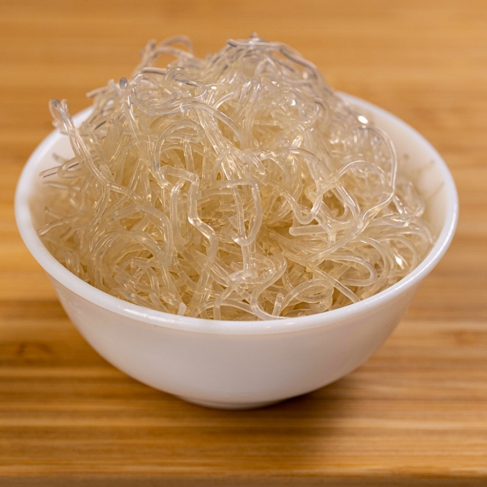 A bowl of noodles in a white bowl on top of a wooden table.