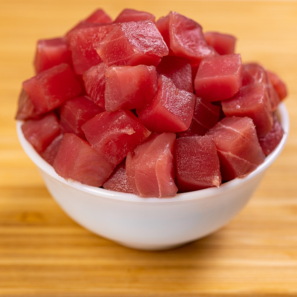 A bowl of tuna cubes on a wooden table.