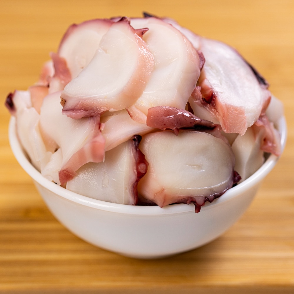 Sliced octopus in a white bowl on a wooden table.