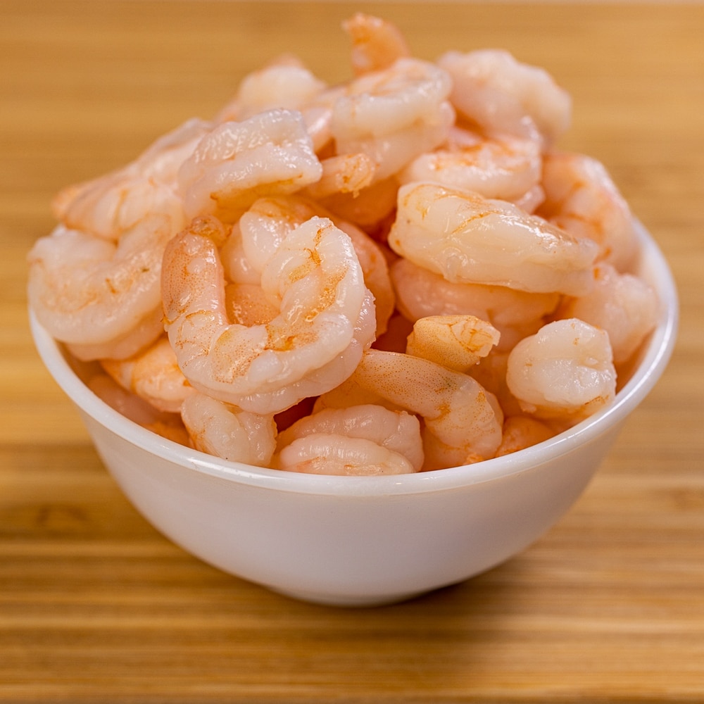 Shrimp in a white bowl on a wooden table.