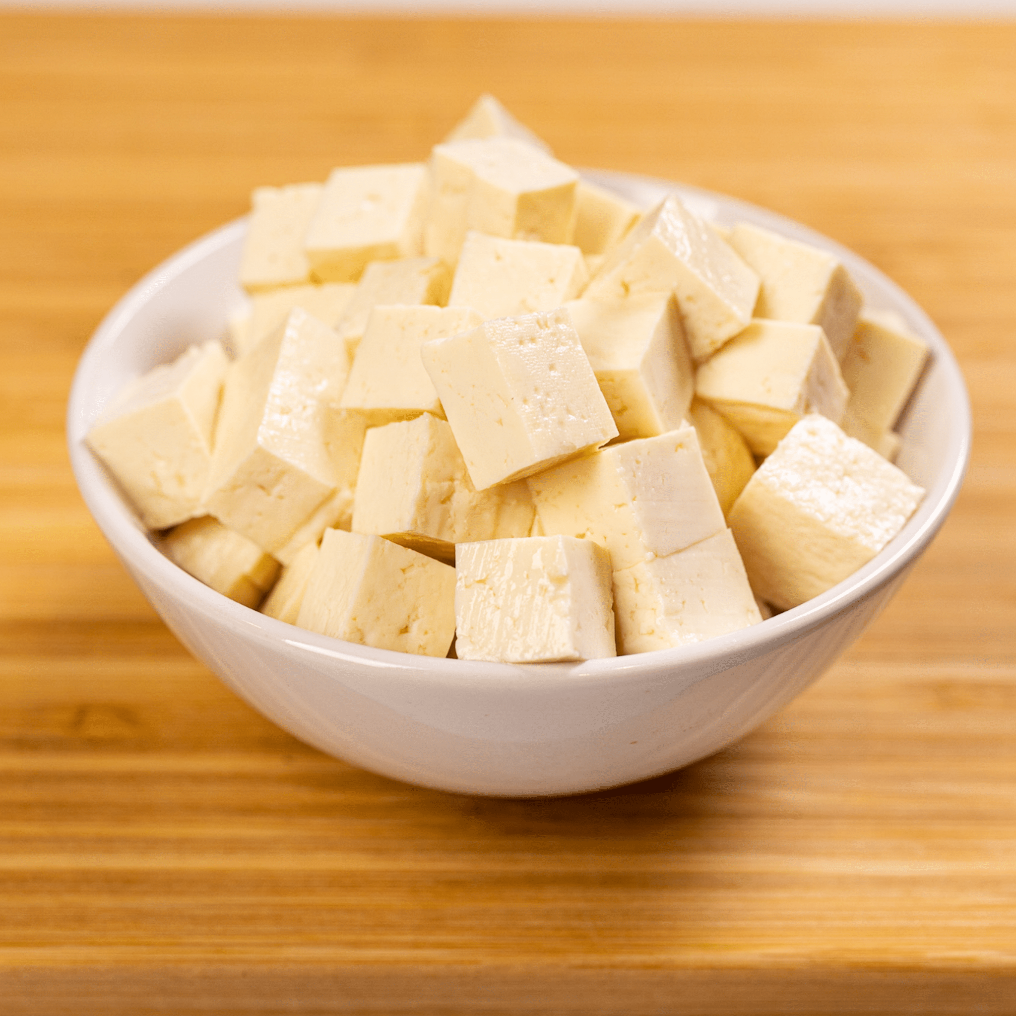 Tofu in a white bowl on a wooden table.
