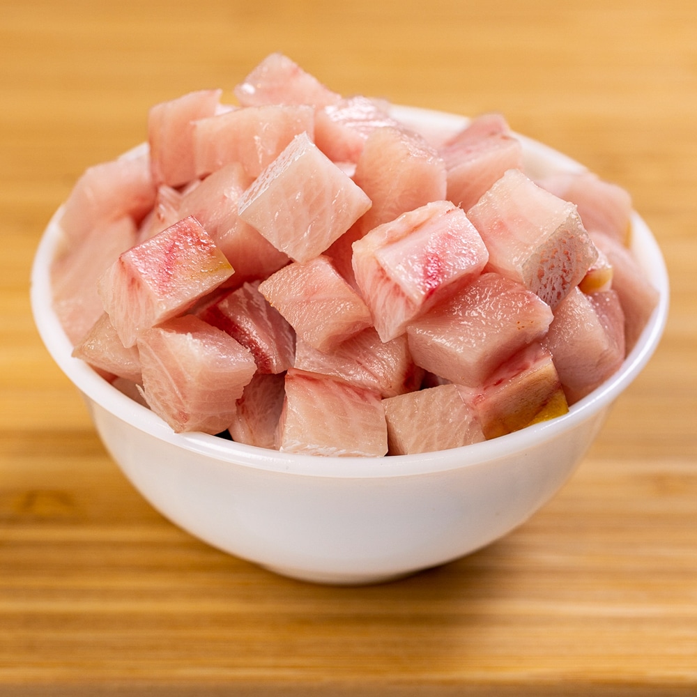 A white bowl of cubed tuna on a wooden table.