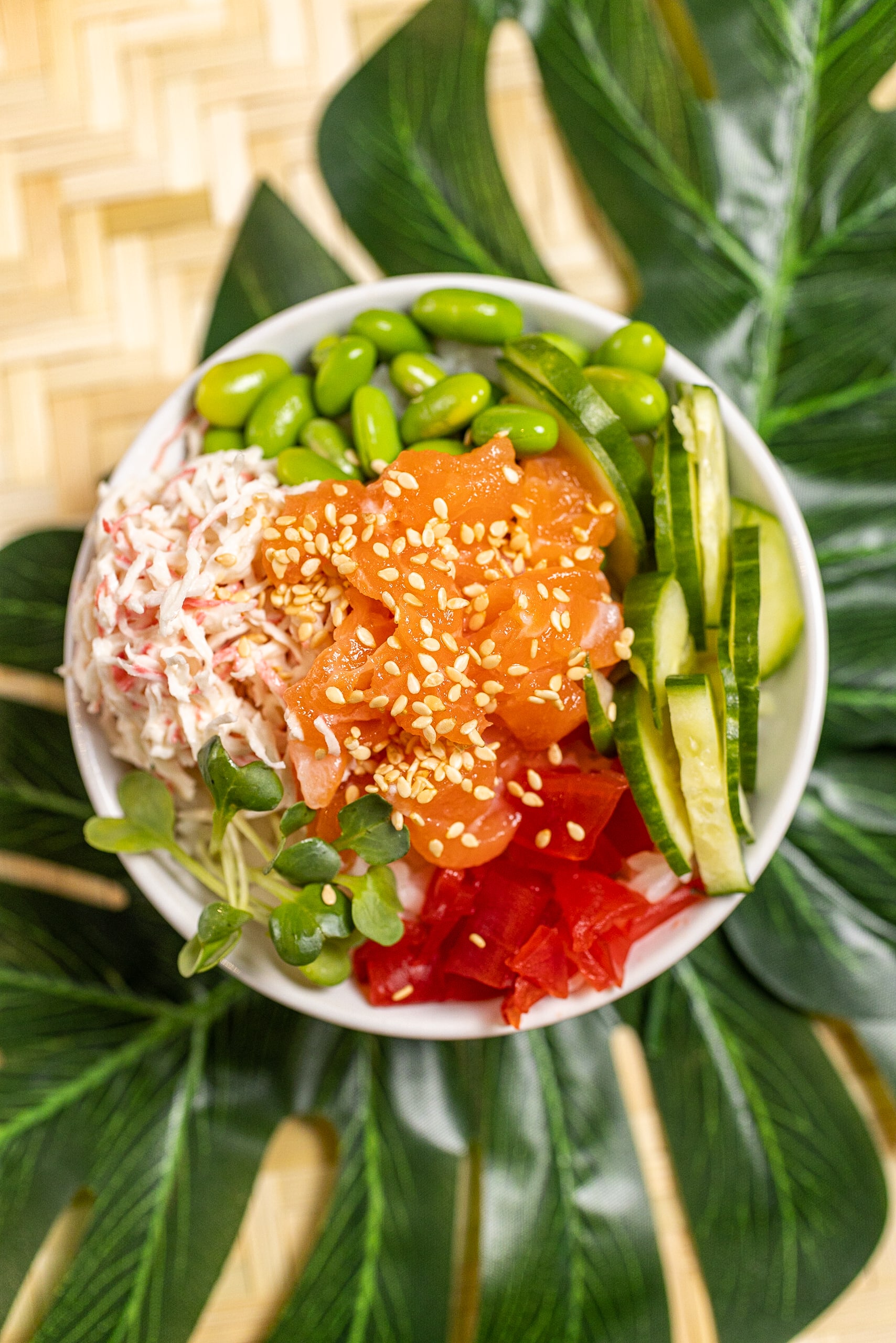 A bowl of sushi and vegetables on top of a leaf.