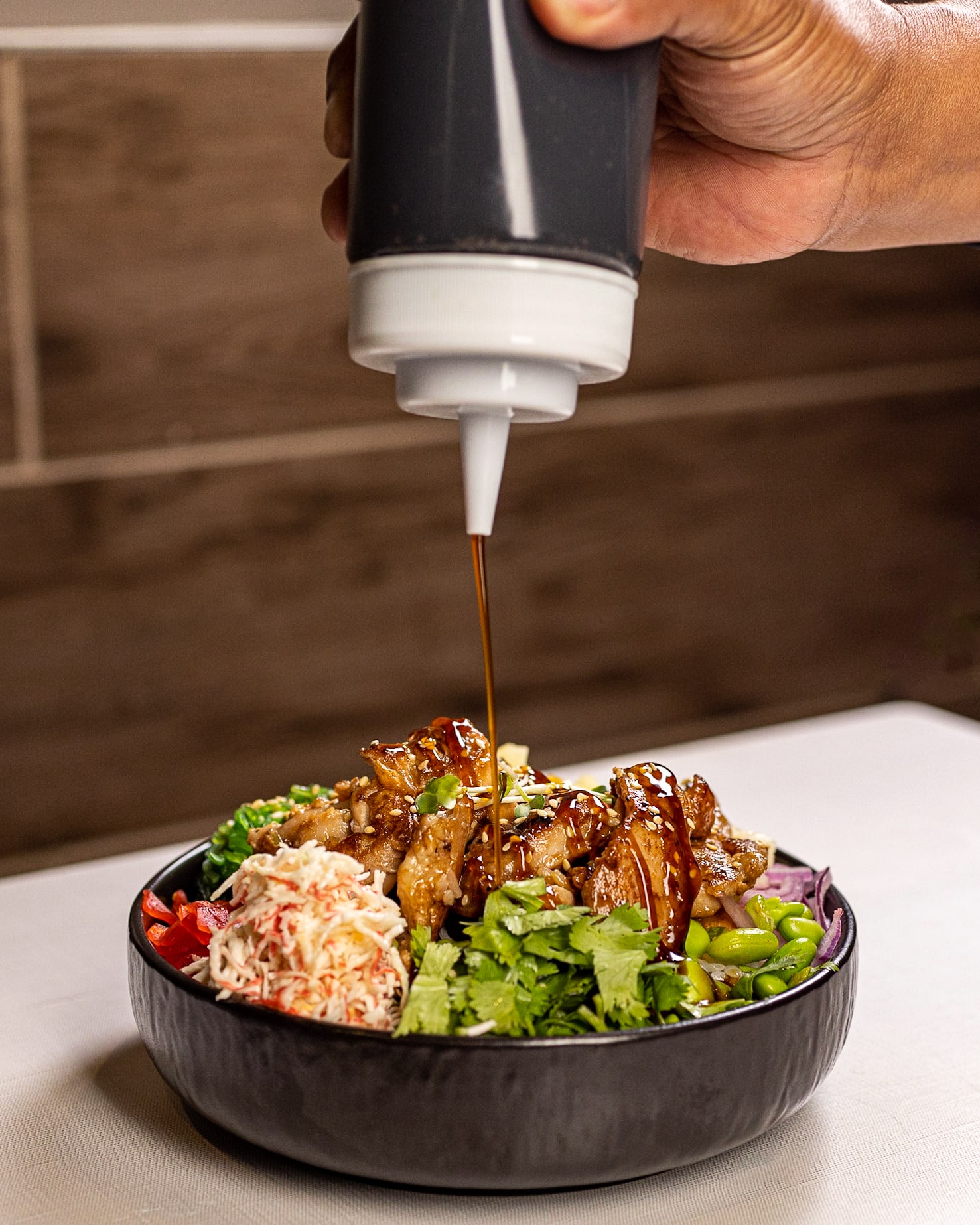 A person pouring sauce on a bowl of salad.
